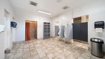 Un bagno pubblico con diversi orinatoi, un cestino e un dispenser di asciugamani.