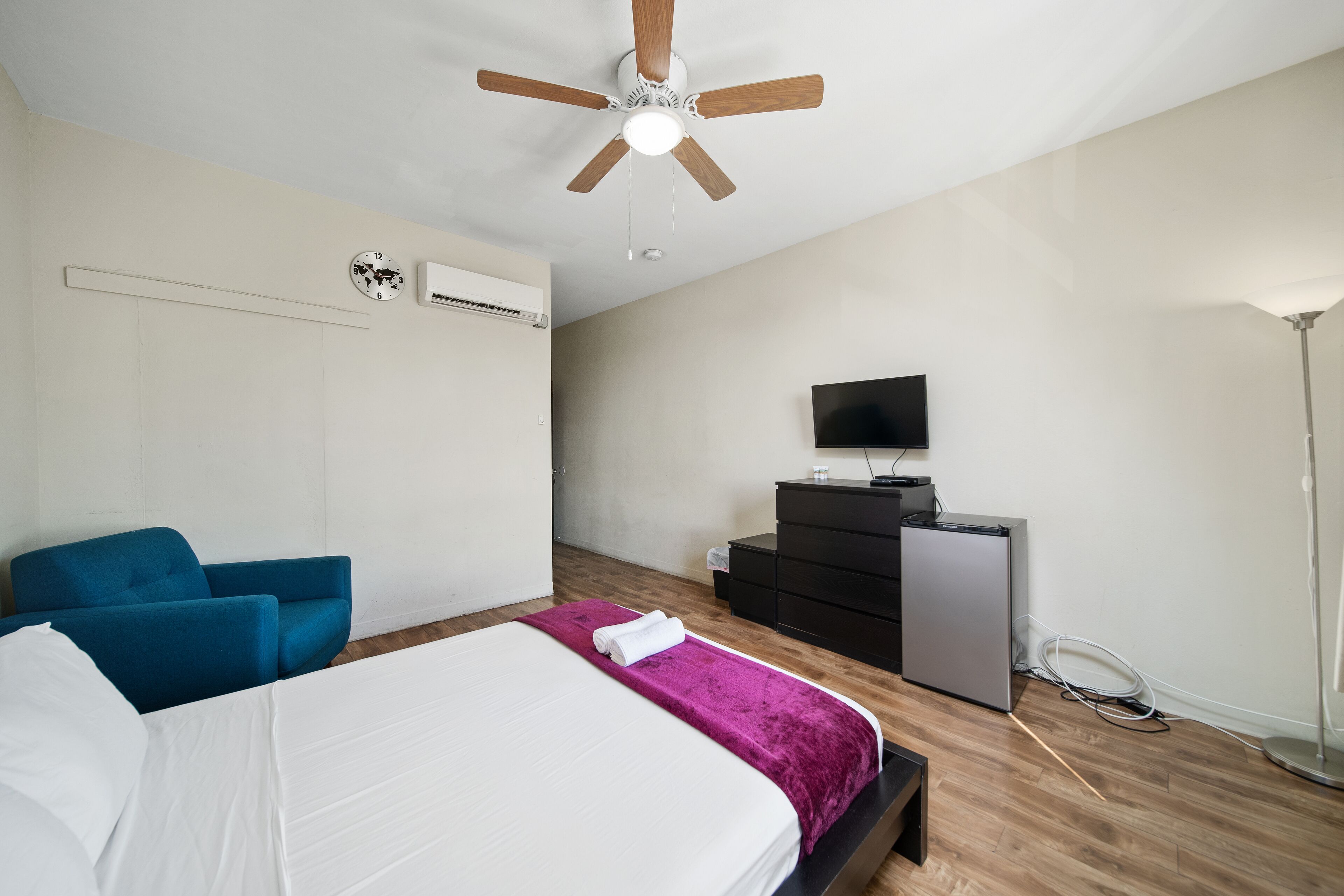 Un dormitorio con cama, ventilador de techo, televisión, cómoda y escritorio.