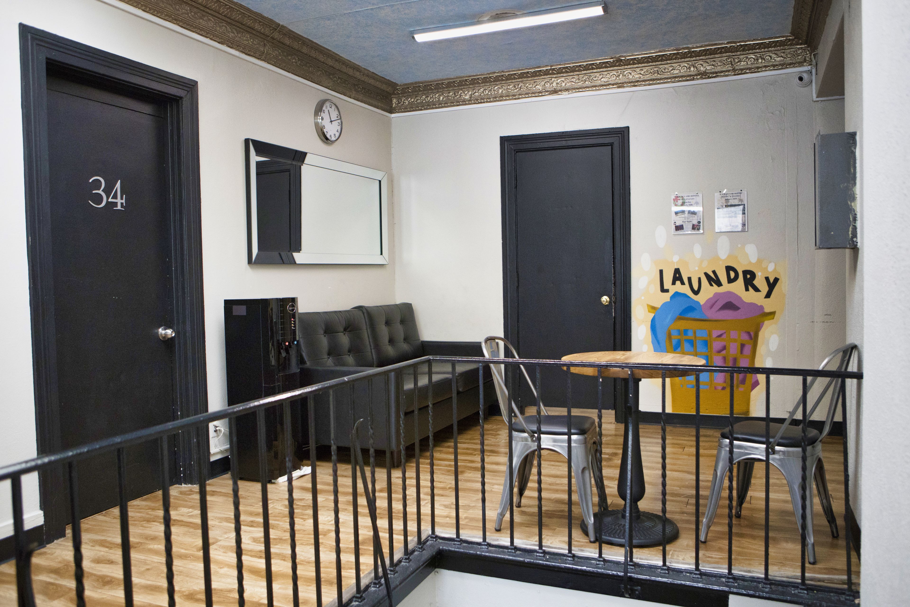 A room with a black door labeled '34', a black sofa, a small table with chairs, and a 'laundry' sign on the wall.