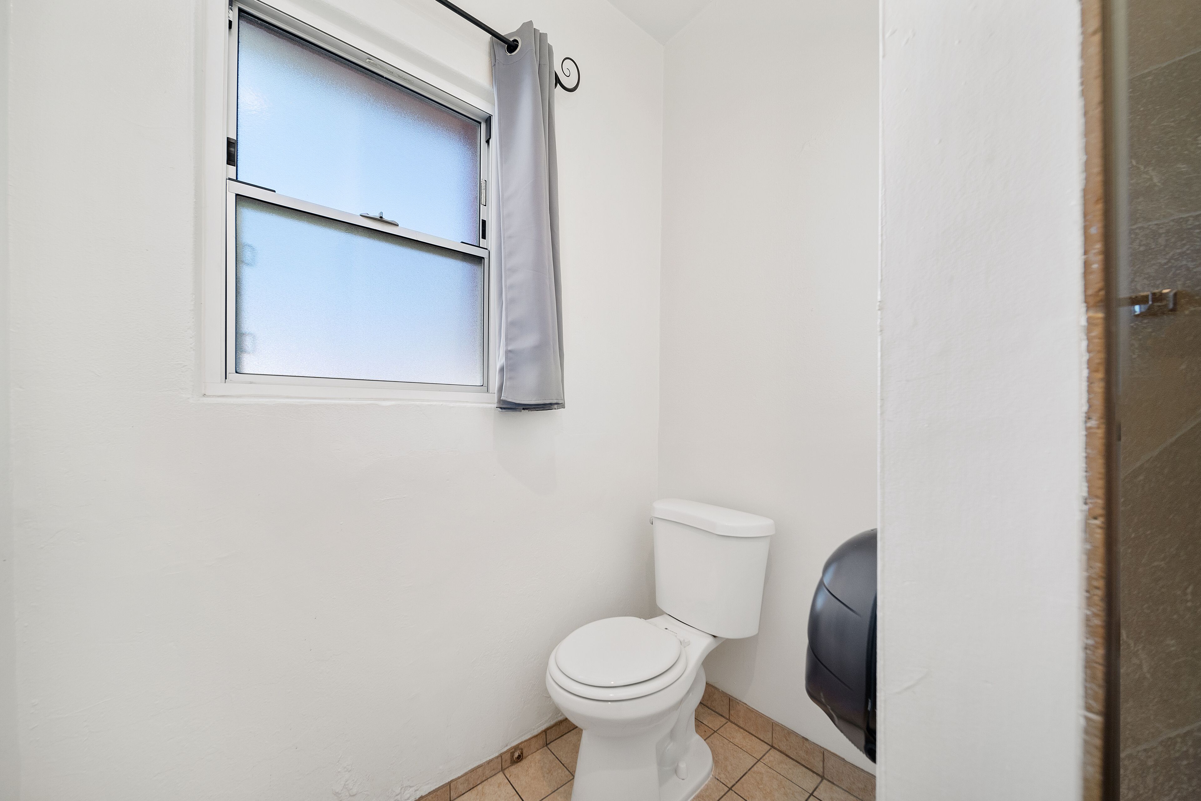 A small, clean bathroom with a toilet, a window with a curtain, and a shower area.