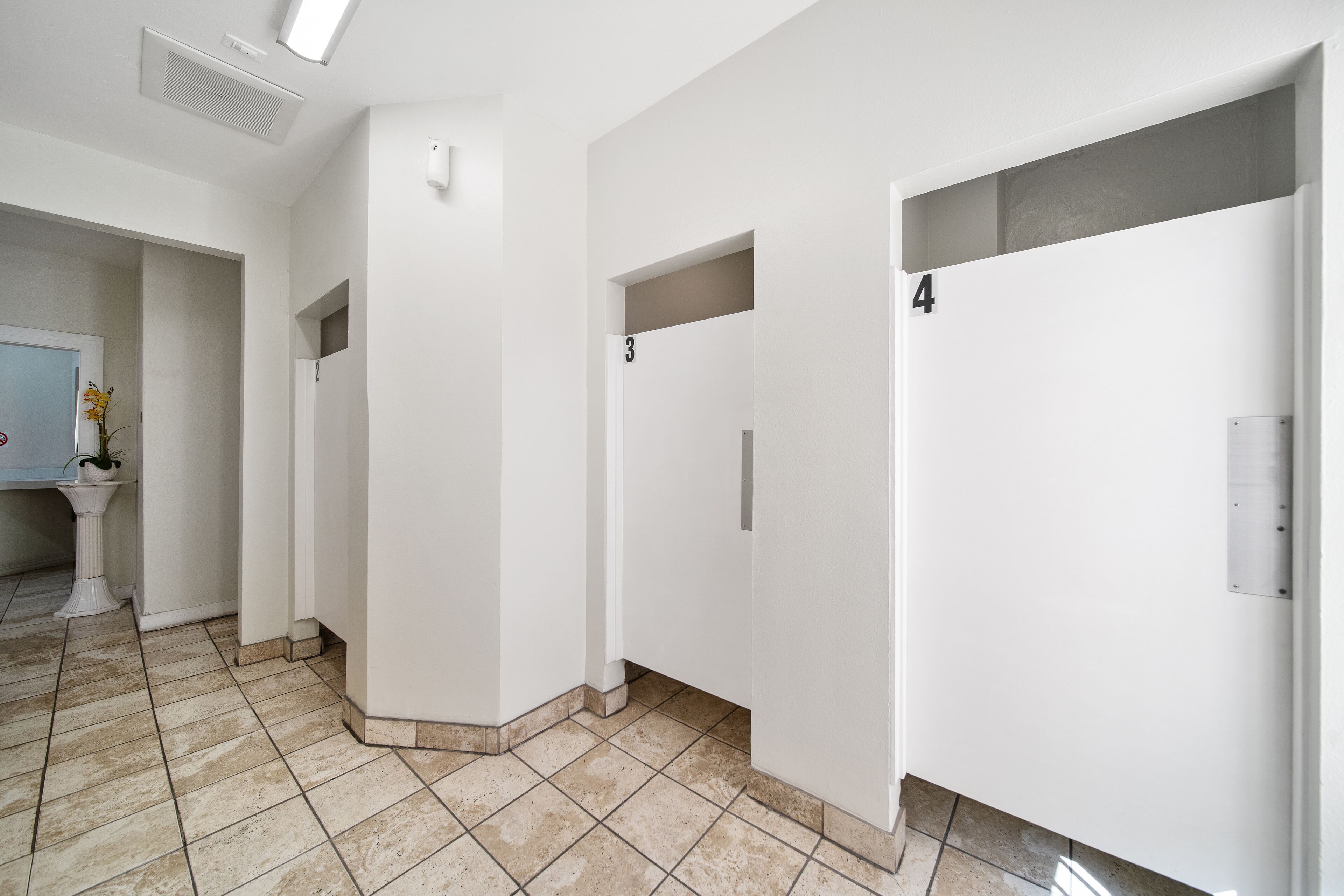 A clean, modern hallway with white walls and tiled flooring, featuring doors numbered 3 and 4.
