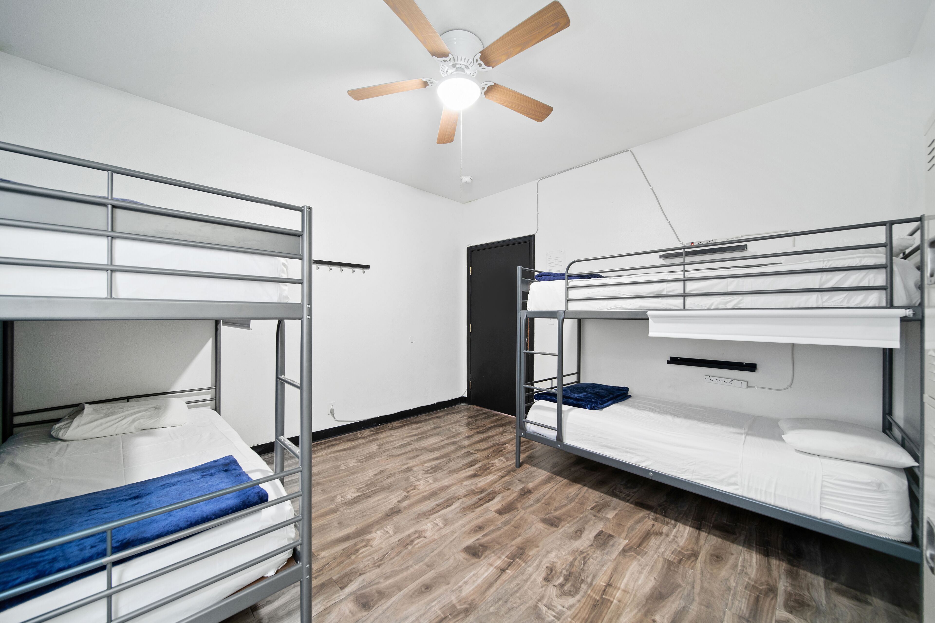 A room with two bunk beds, a ceiling fan, and a wooden floor.