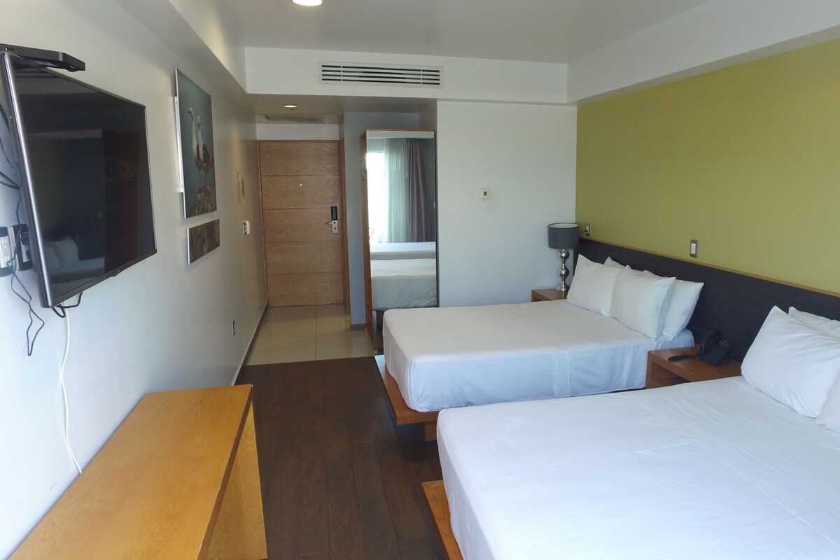 A hotel room with two beds, a TV, a desk, and a door leading to a bathroom.