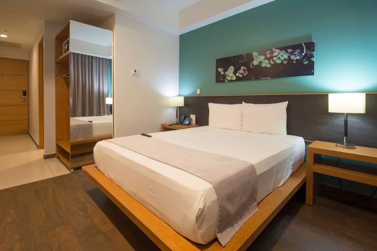 A modern hotel room with a large bed, bedside tables, a mirror, and a wall-mounted artwork.