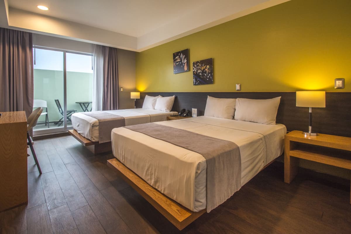 A hotel room with two beds, a desk, and a balcony with a chair.