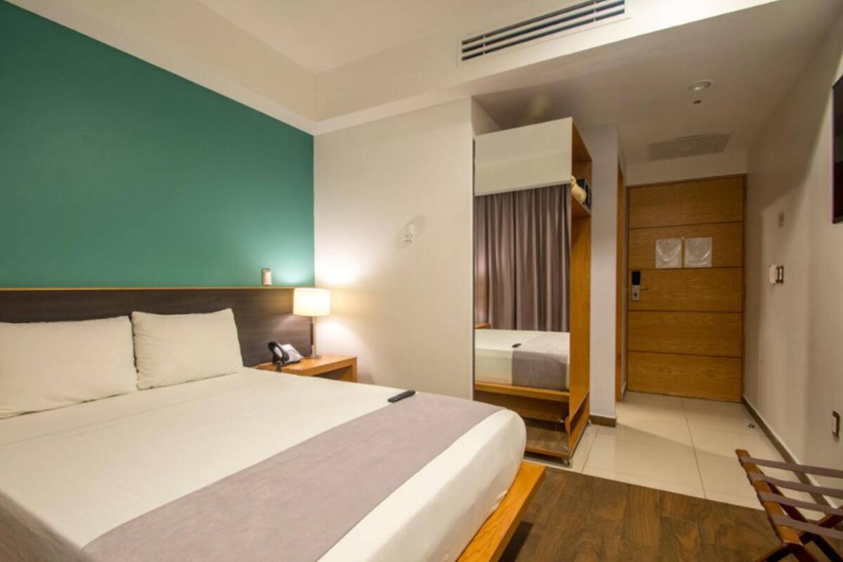 A hotel room with a bed, bedside table, lamp, and a view of the hallway.