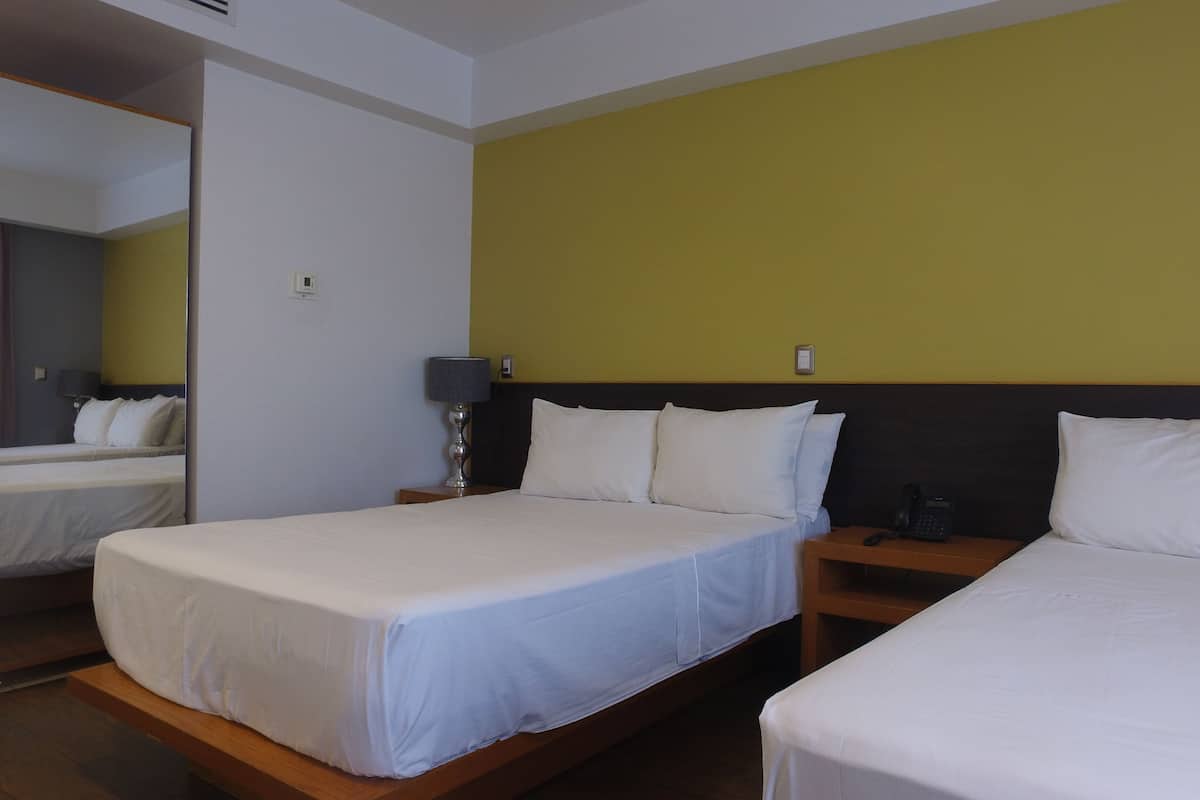 A hotel room with two beds, a bedside table with a lamp, a phone, and a mirror.