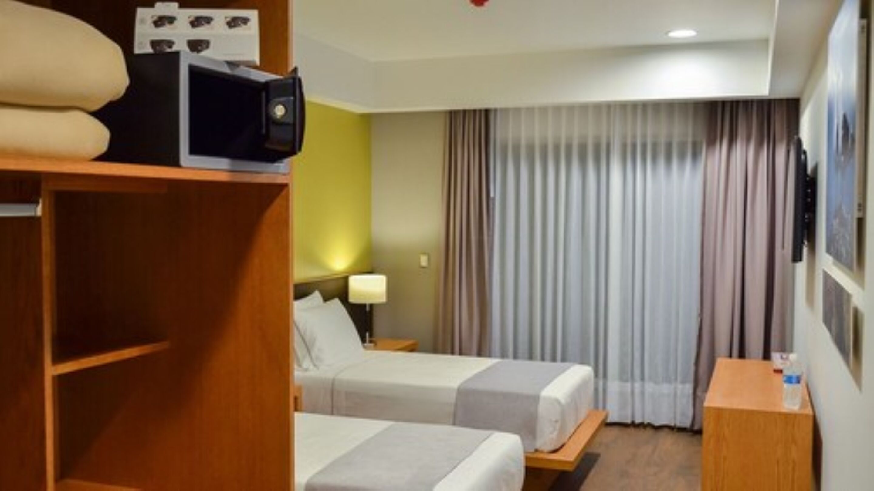 A hotel room with two beds, a wooden wardrobe, a desk with a lamp, and a television.