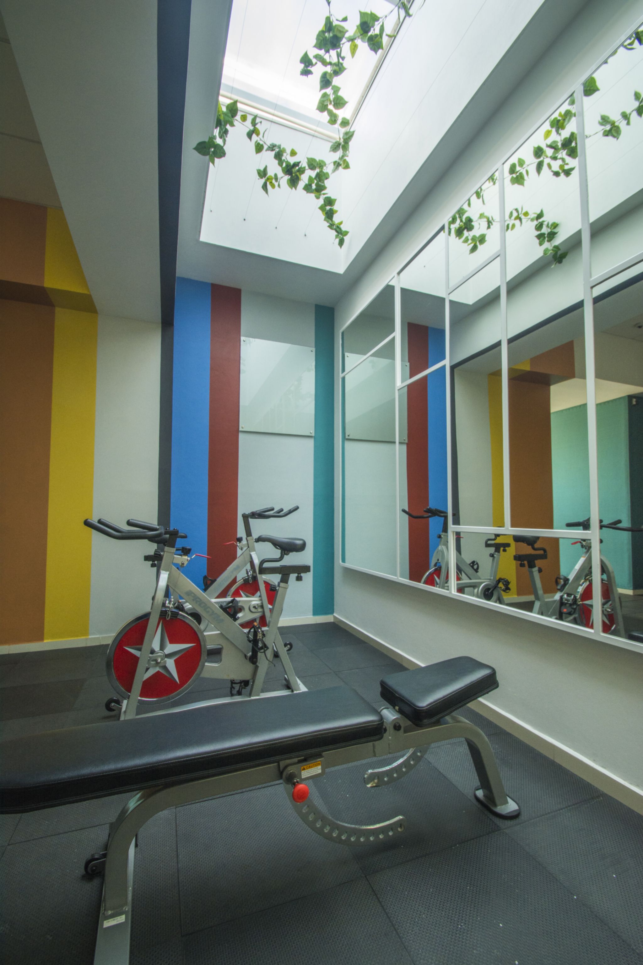 A gym with exercise equipment, a bench, and a large mirror.