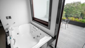 Un baño moderno con una bañera grande, una ventana con persianas y un balcón con una silla y barandilla.