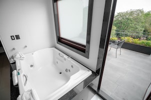 Un baño moderno con una bañera grande, una ventana con persianas y un balcón con una silla y barandilla.