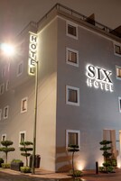 Un hotel llamado 'SIX HOTEL' con una fachada moderna, múltiples ventanas y una entrada bien iluminada.