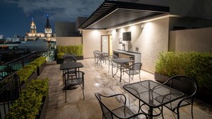 Un patio al aire libre con mesas y sillas, un área de estar techada y una vista de un edificio histórico al fondo.