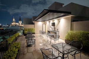 Un patio al aire libre con mesas y sillas, un área de estar techada y una vista de un edificio histórico al fondo.
