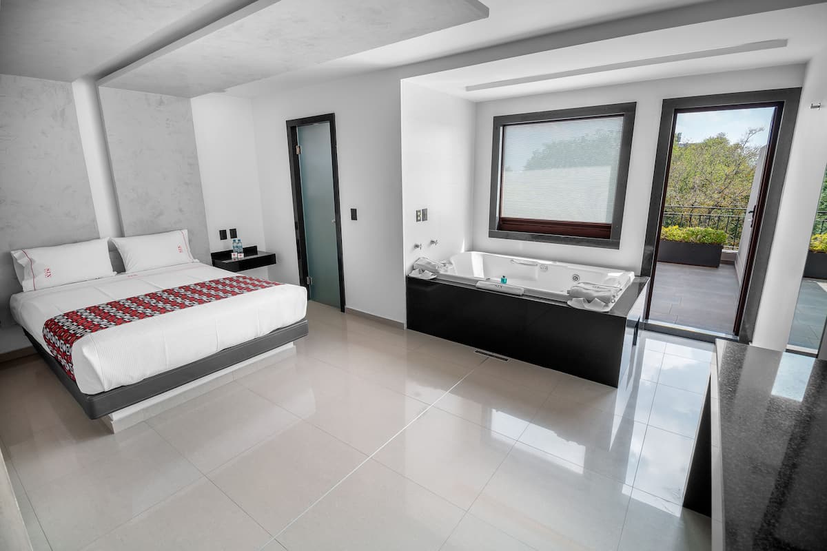 Une chambre moderne avec un grand lit, une baignoire intégrée et un balcon offrant une vue sur les arbres.