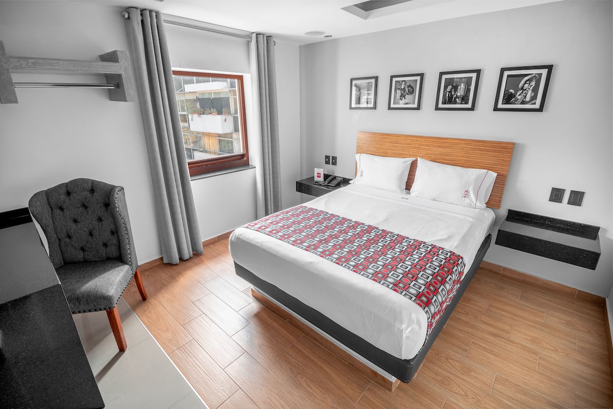 Une chambre d’hôtel avec un lit, une chaise, une table de chevet et une fenêtre avec des rideaux.