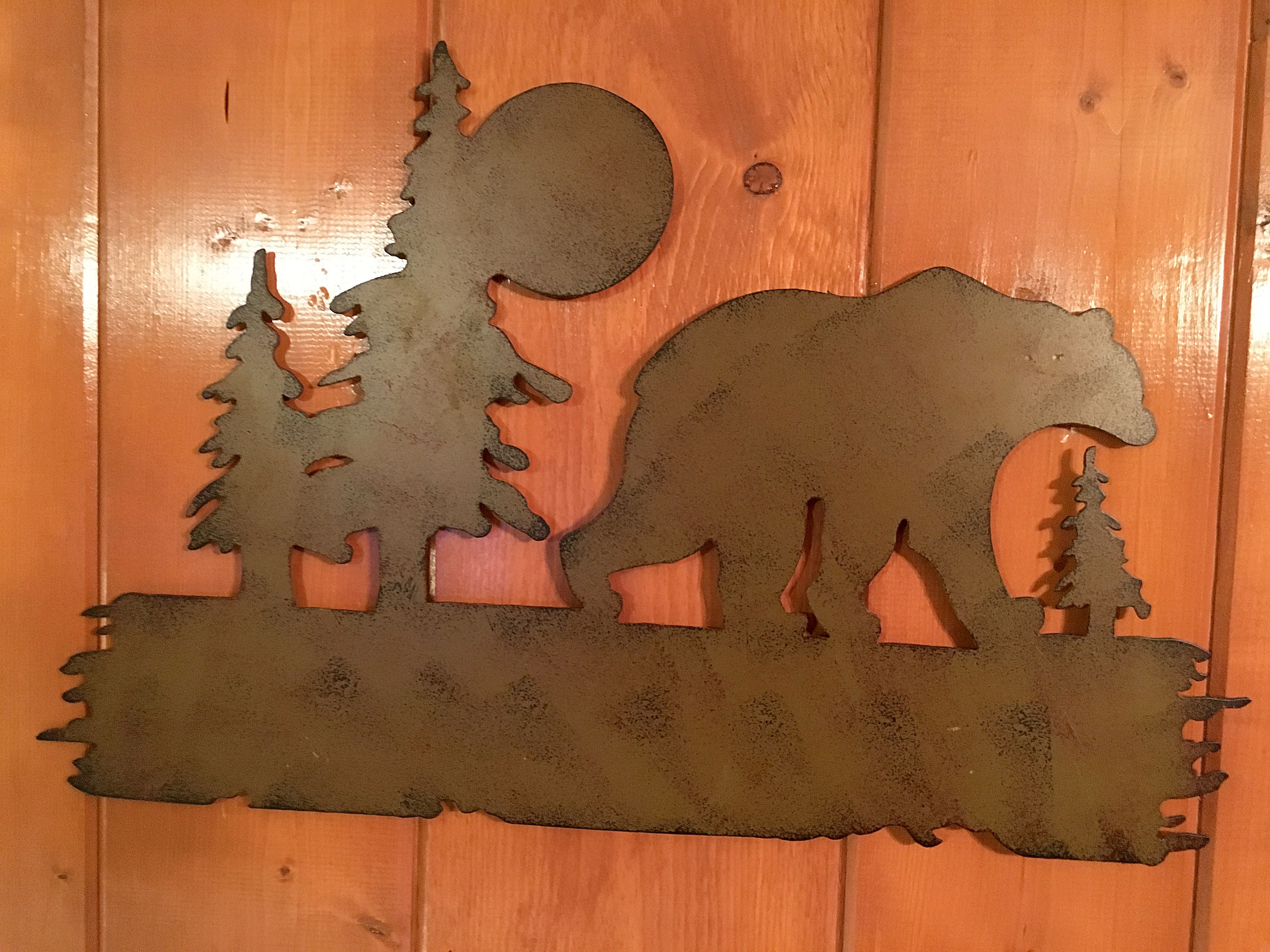 A metal cutout of a bear, trees, and a moon on a wooden background.