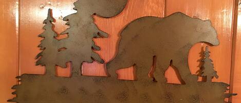 A metal cutout of a bear, trees, and a moon on a wooden background.