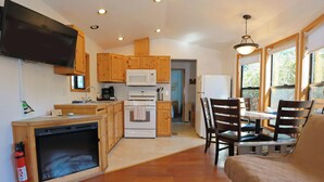 A compact kitchen with wooden cabinets, a microwave, stove, and a dining area with chairs and a table. - Park Motel and Cabins (Florence)