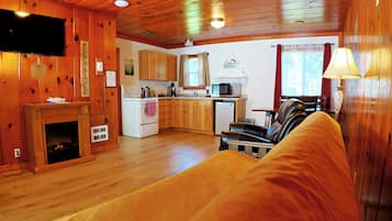 A wooden cabin interior with a living area, kitchen, fireplace, and a television.