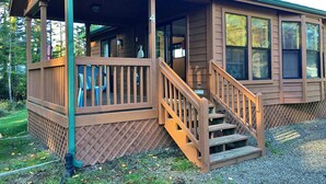 A wooden cabin with a covered porch, a staircase, and a view of the surrounding forest. - Park Motel and Cabins (Florence)