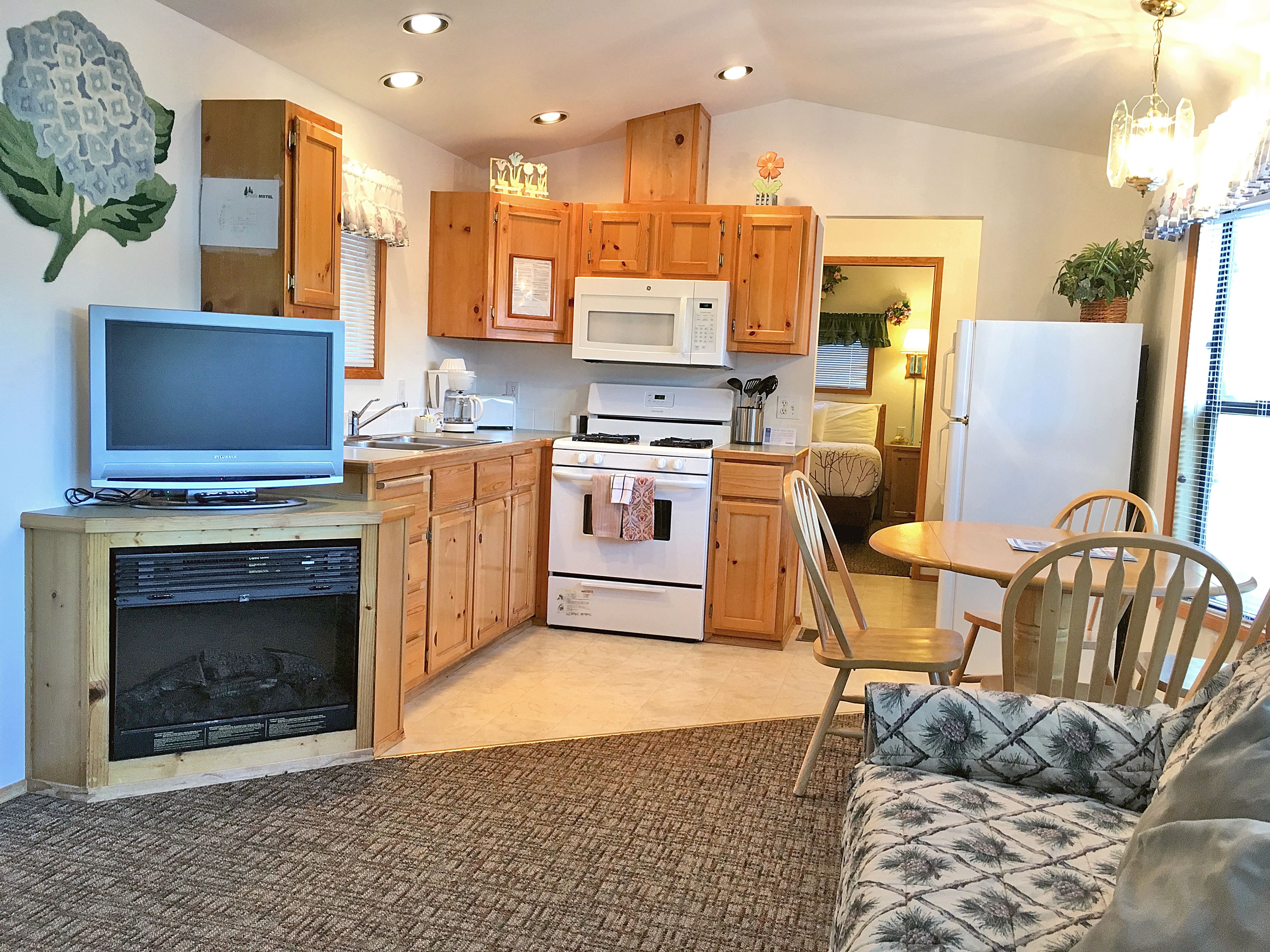 A compact kitchen with wooden cabinets, a microwave, stove, and a television on a stand.