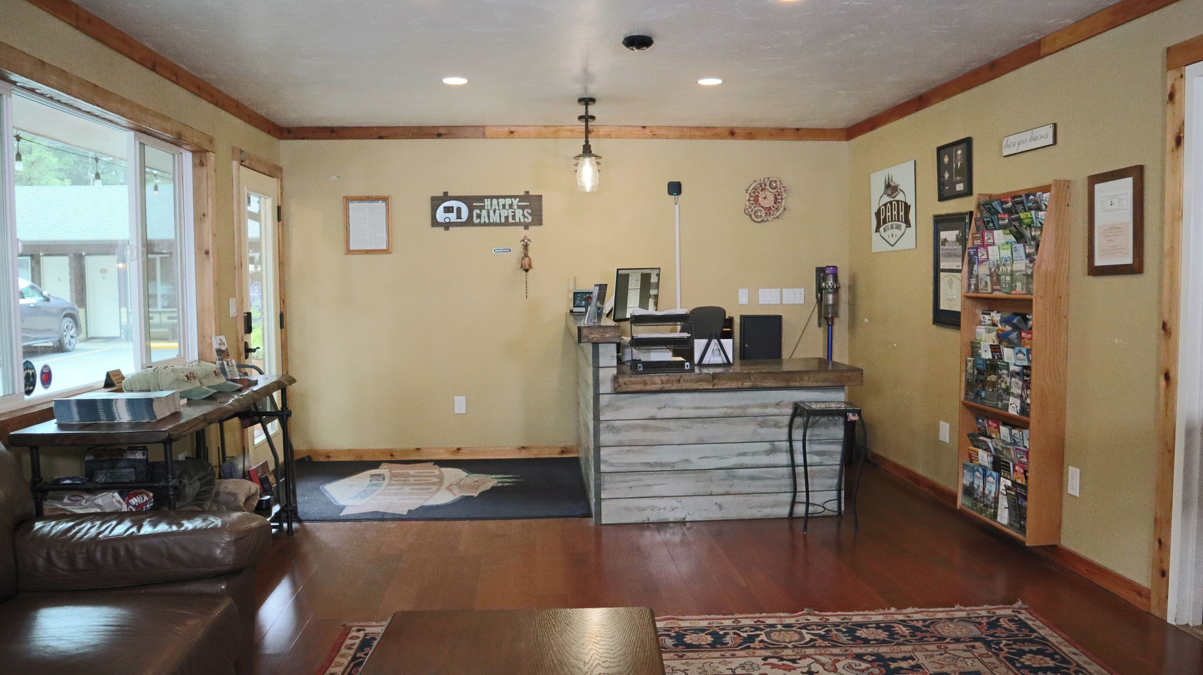 A reception area with a desk, a computer, a printer, a bulletin board, and a window with a view of the outside.