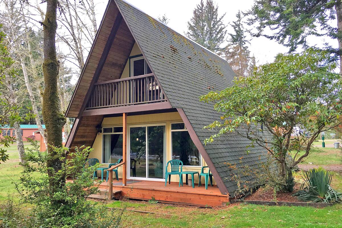 A small, A-frame cabin with a balcony and a porch area.