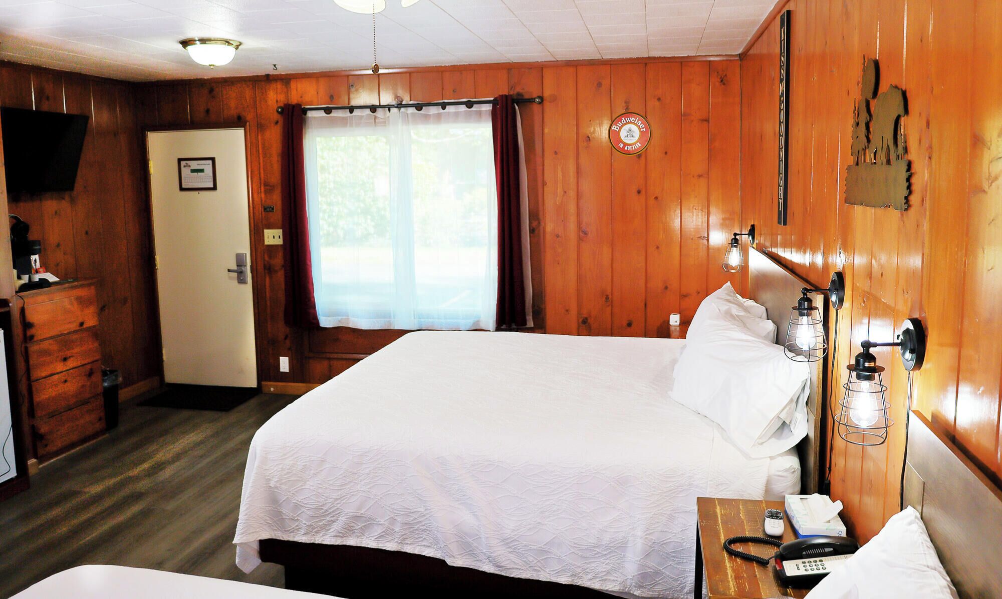 Habitación tipo King Queen Quad con una cama, lámpara de noche y una pared de madera con un reloj.