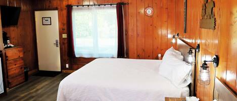Habitación tipo King Queen Quad con una cama, lámpara de noche y una pared de madera con un reloj.