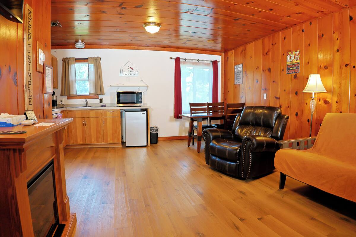 A wooden cabin interior with a kitchen, dining area, and seating.