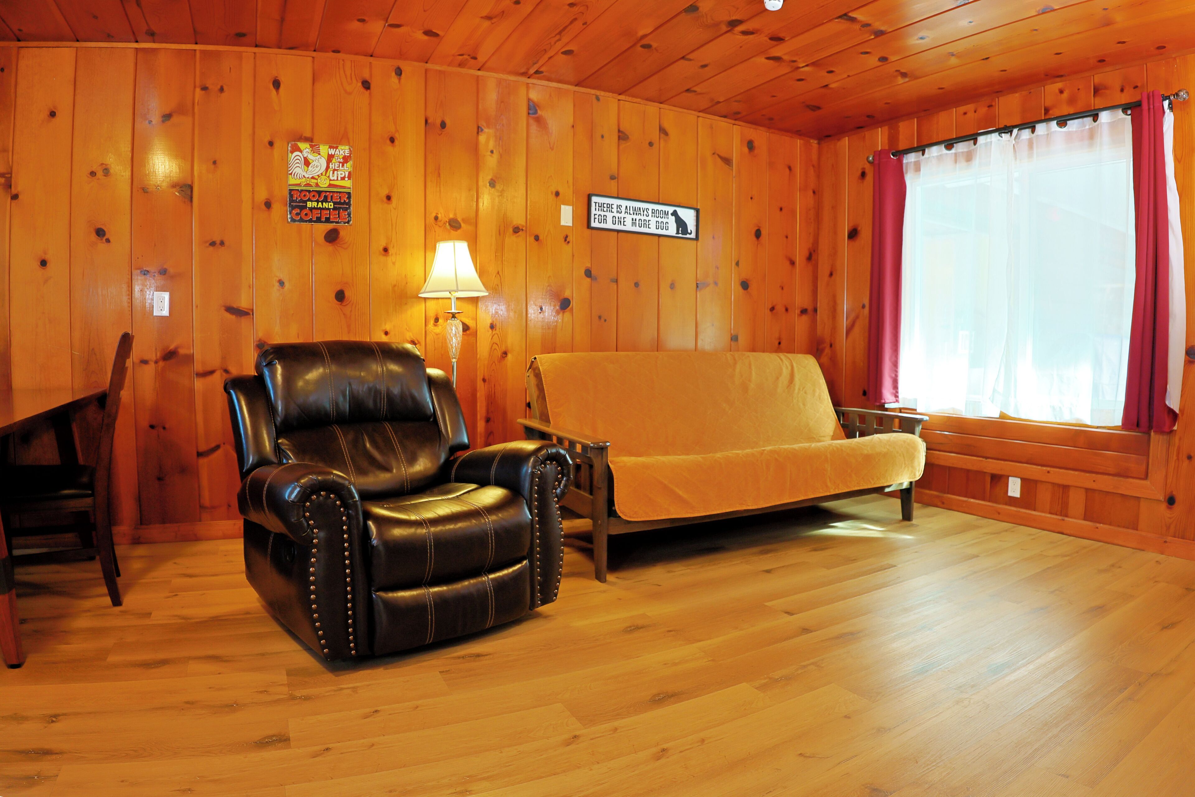 A room with wooden walls, a leather armchair, a sofa, a lamp, and a sign on the wall.