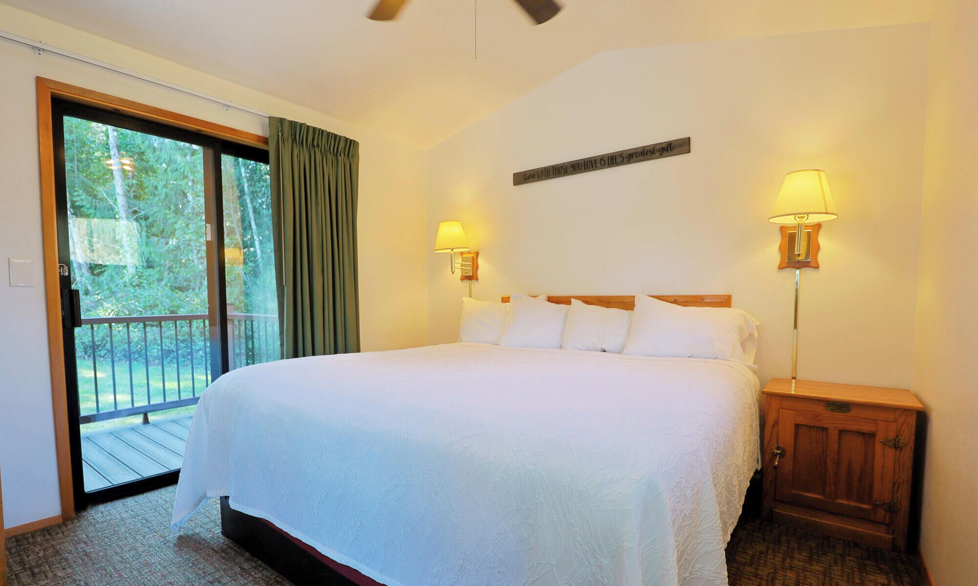 Habitación de hotel con una cama grande, dos lámparas de noche, una mesita de noche de madera, un ventanal corredero a un balcón y un cartel en la pared.