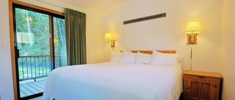 Habitación de hotel con una cama grande, dos lámparas de noche, una mesita de noche de madera, un ventanal corredero a un balcón y un cartel en la pared.