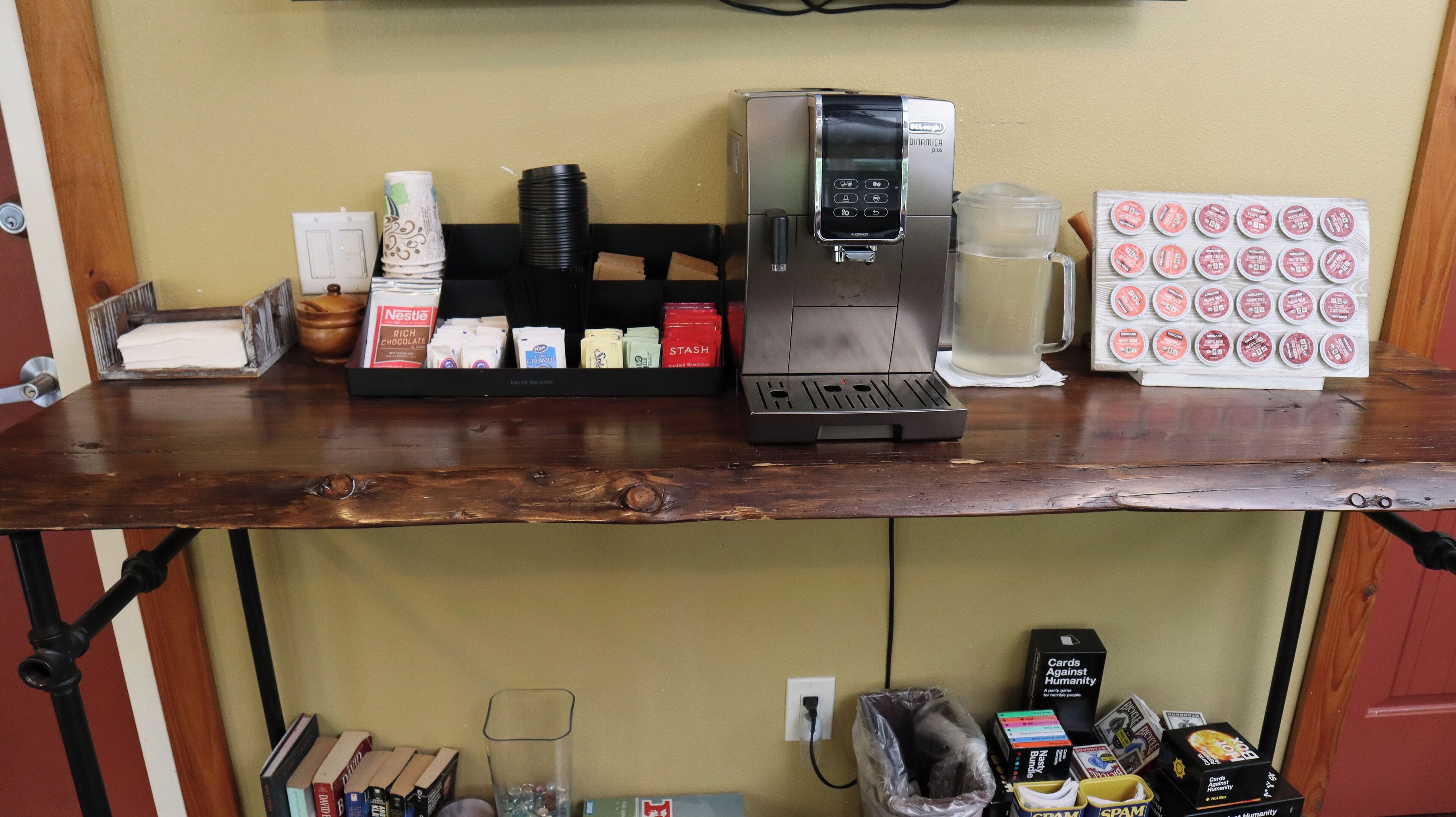 Een koffieapparaat, een stapel wegwerpbekers en een doos koffiecups op een houten toonbank.
