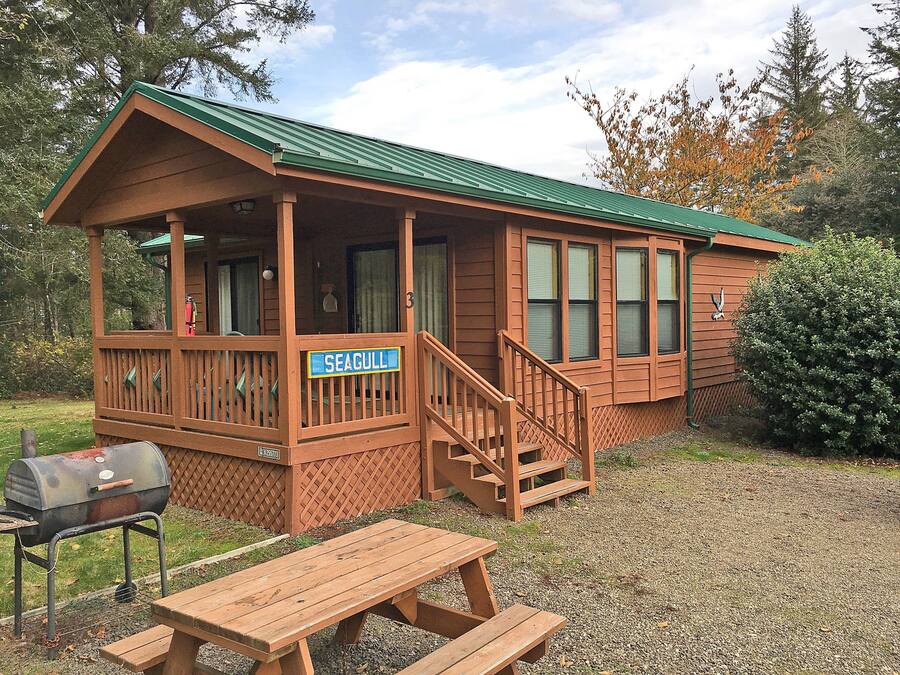 A wooden cabin with a porch, a covered picnic table, and a barbecue grill.
