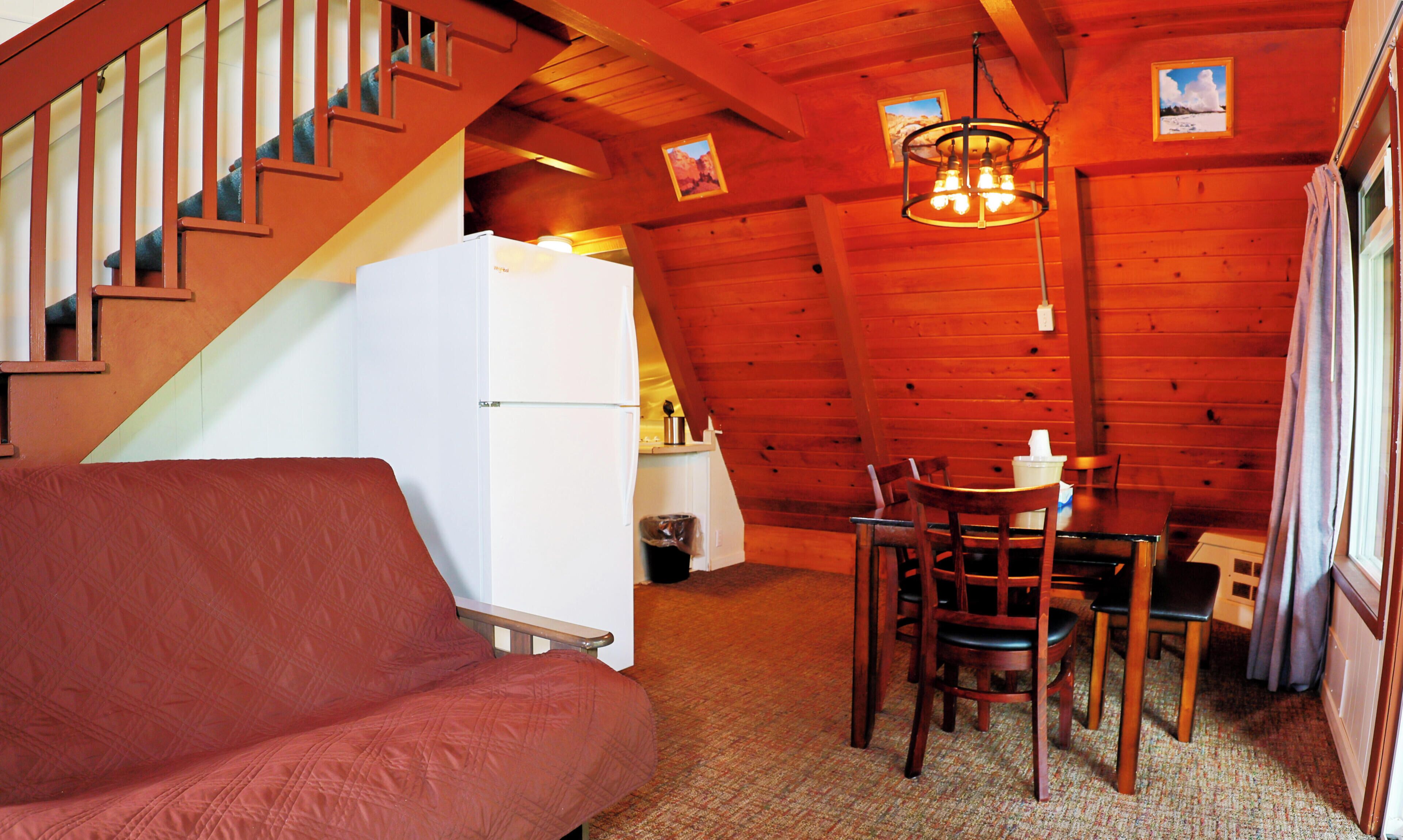 A cozy room with a wooden ceiling, a dining table with chairs, a white refrigerator, and a staircase.