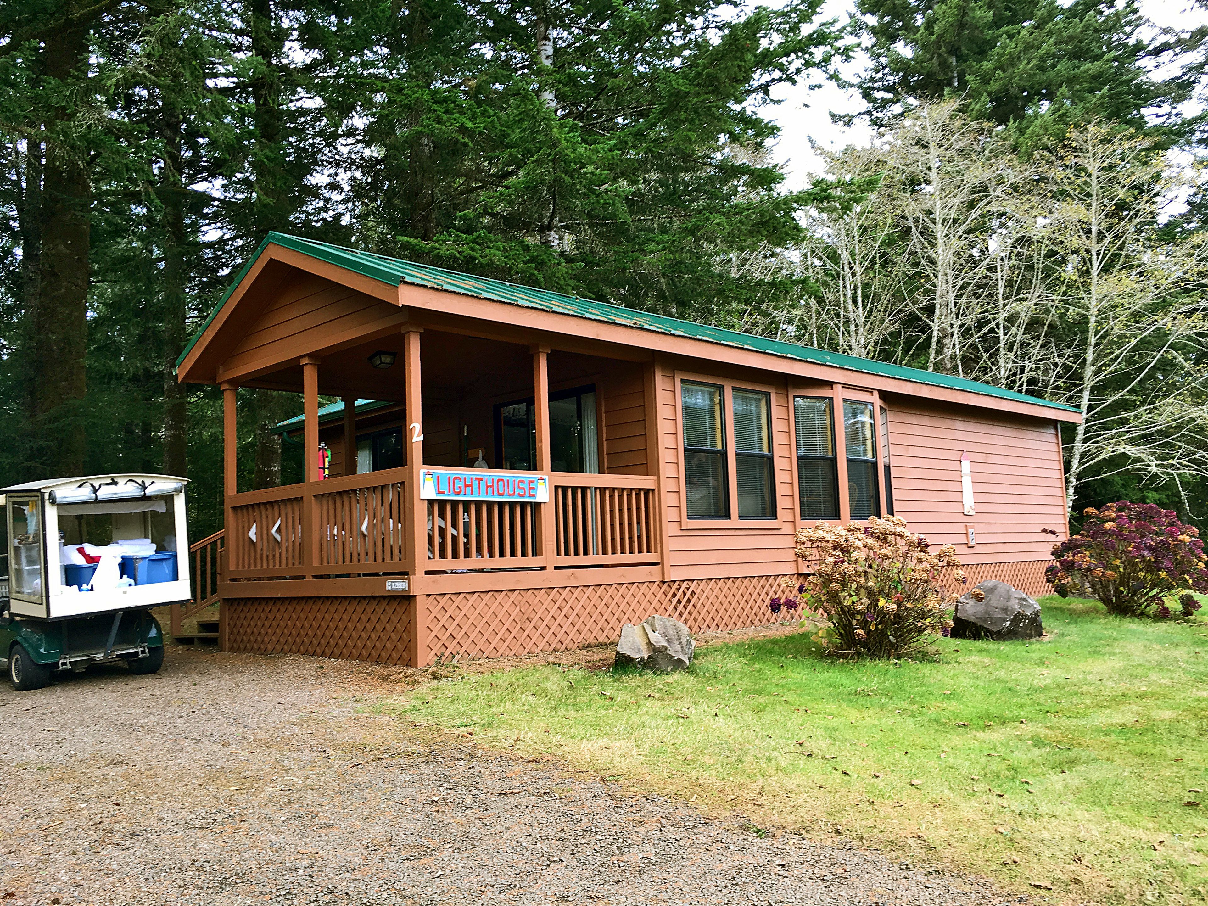 A wooden cabin with a porch, a sign reading "LIGHTHOUSE", and a small truck parked in front.