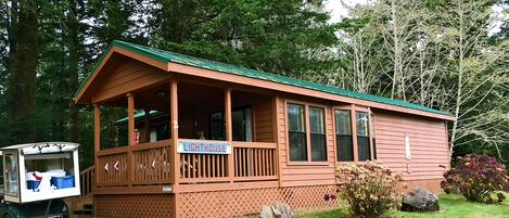 A wooden cabin with a porch, a sign reading "LIGHTHOUSE", and a small truck parked in front.