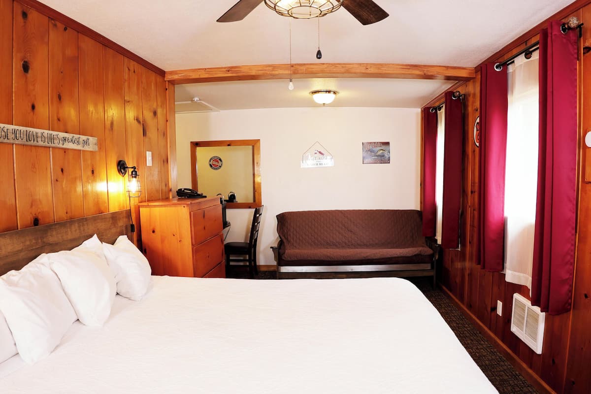 A wooden room with a bed, a desk, a chair, a ceiling fan, and a thermostat.