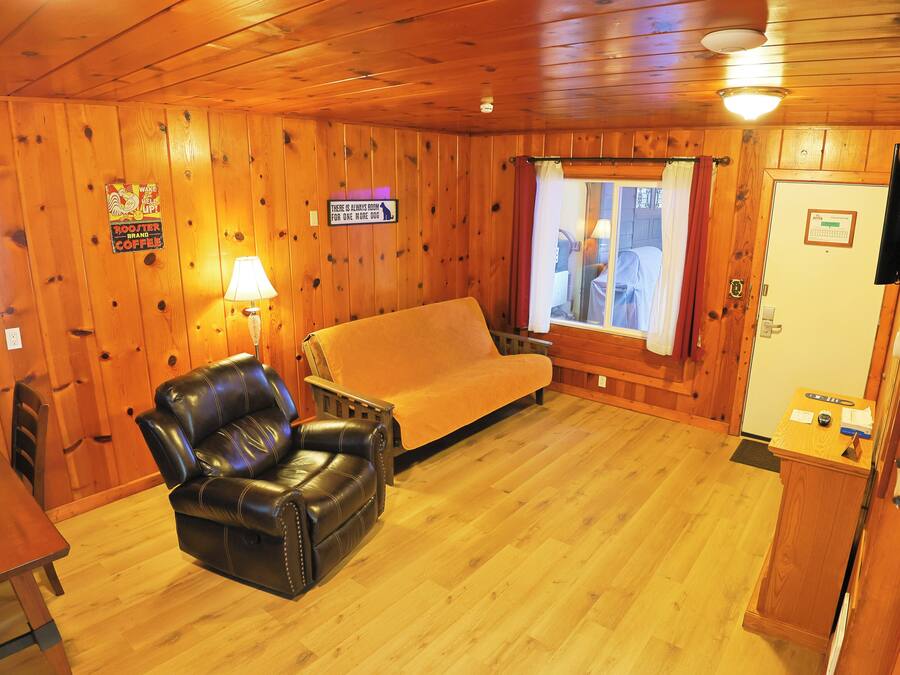 Een kamer met houten lambrisering, een leren fauteuil, een bank, een tafel en een aan de muur bevestigde televisie.