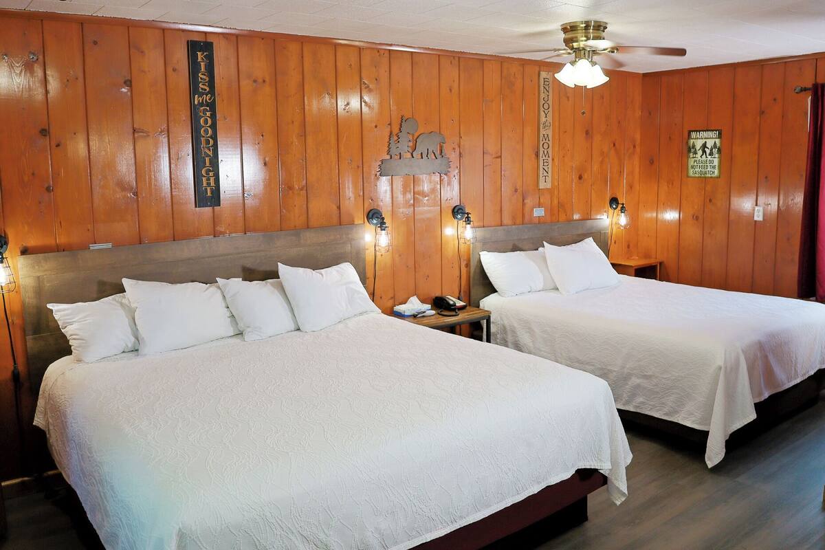 A King Queen Quad with two beds, wooden walls, a ceiling fan, and a warning sign.
