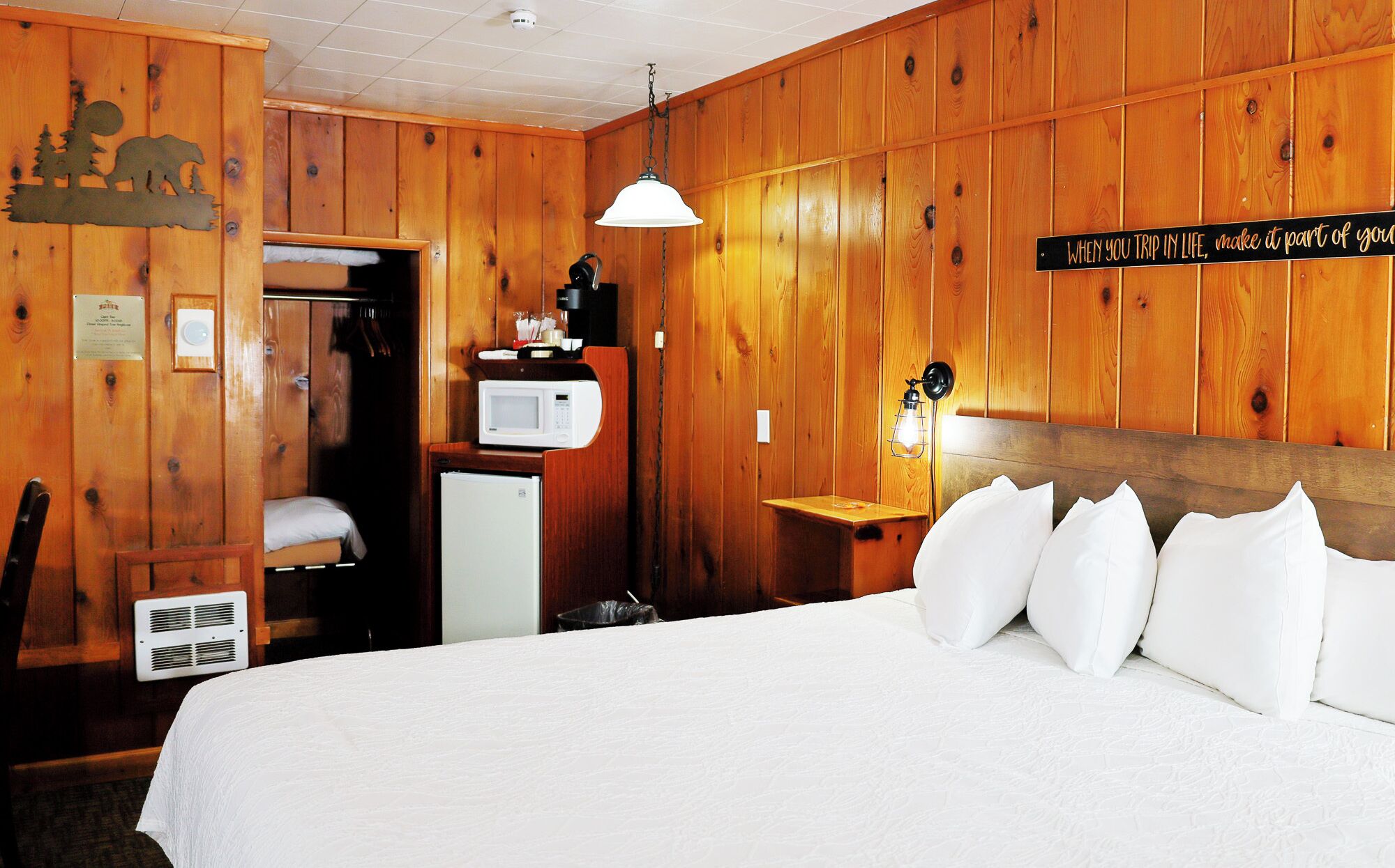 Una habitación de madera con una cama, un microondas, un refrigerador pequeño y un cartel en la pared.
