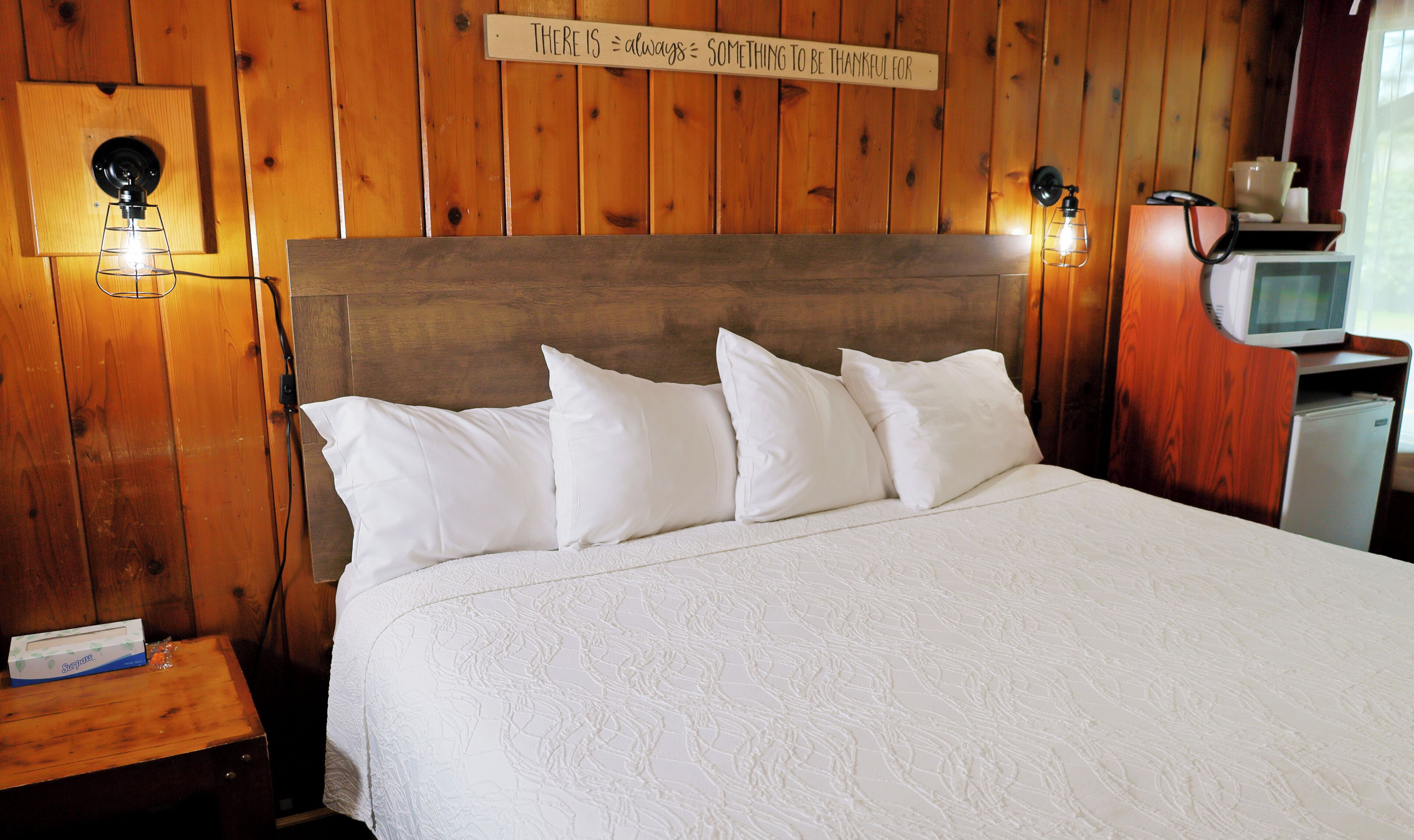 A wooden-paneled room with a bed, a sign above the bed, and a small table with a box.