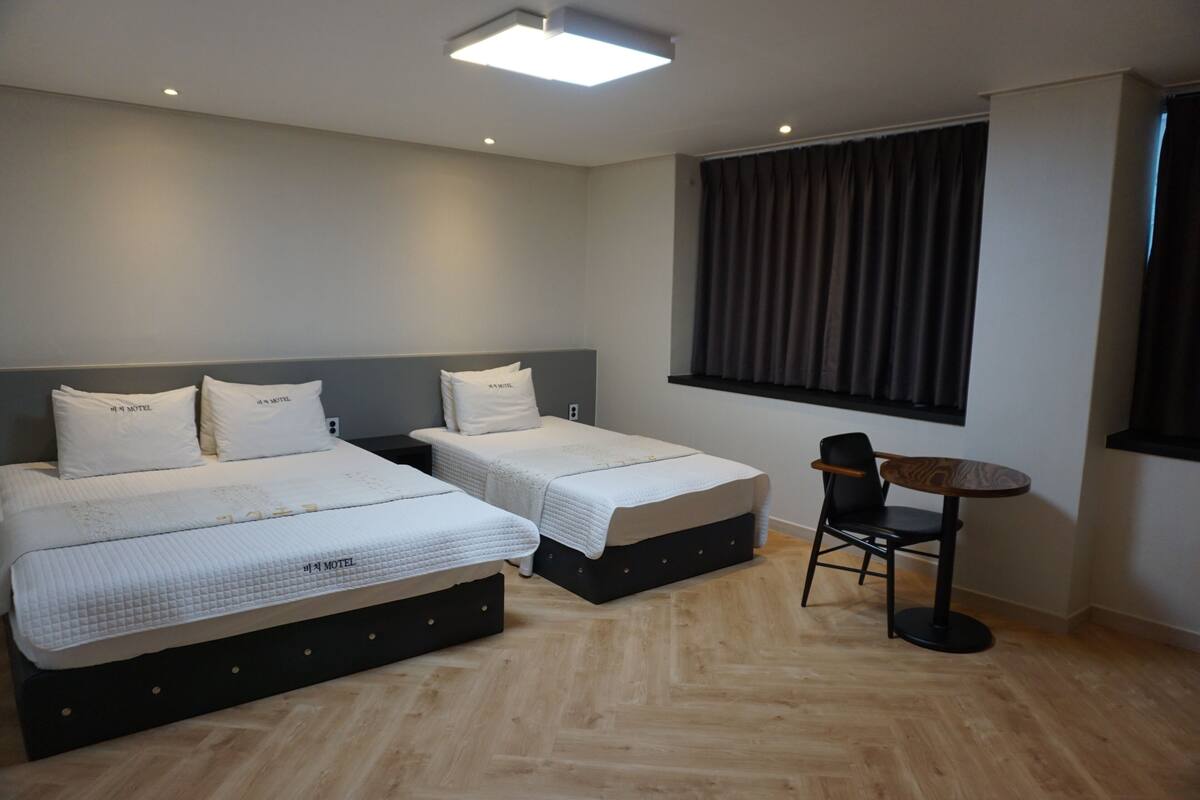 A hotel room with two beds, a small table, and a chair.