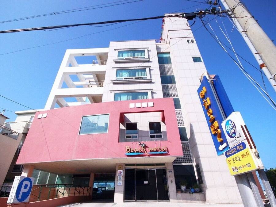 Un immeuble à plusieurs étages dont une partie, de couleur rose vif, est clairement identifiable et porte l’inscription « Beach Motel ».
