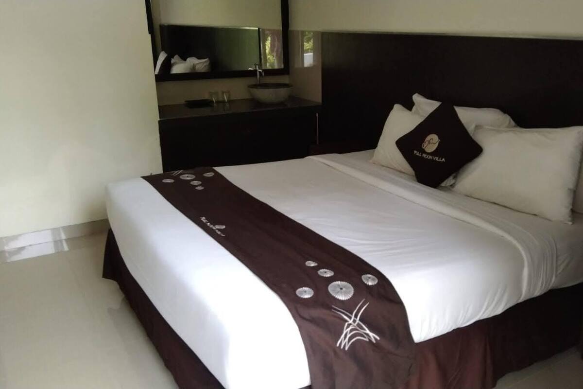 A neatly made bed with a white and brown bedspread, a headboard, and a pillow with a logo.