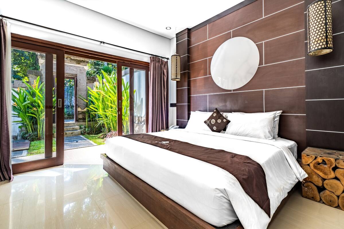 A modern bedroom with a large bed, a view of a garden, and a stone wall.
