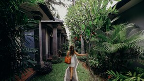 Un sendero atraviesa un exuberante jardín con plantas tropicales y un edificio de columnas.