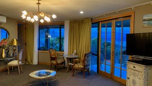 Una habitación de hotel con un ventanal grande, un candelabro, un televisor y una zona de comedor.